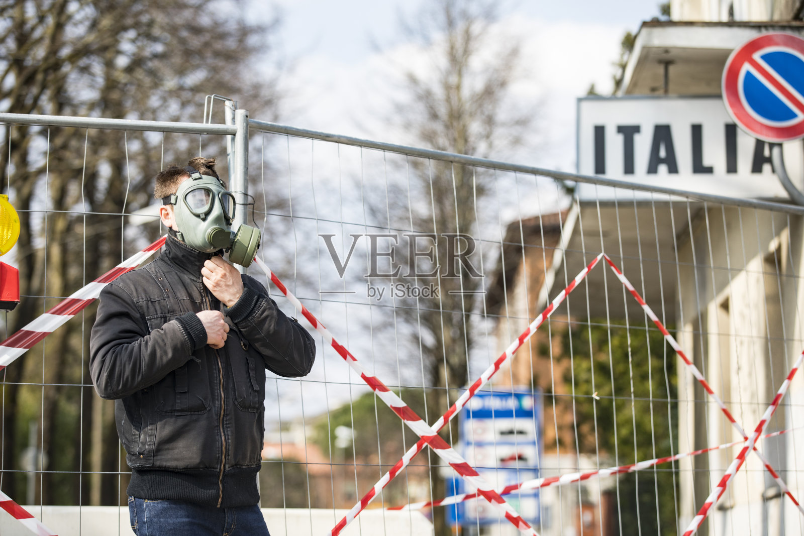 由于冠状病毒，戴口罩的年轻成年男子站在与意大利关闭的边境旁-库存照片照片摄影图片