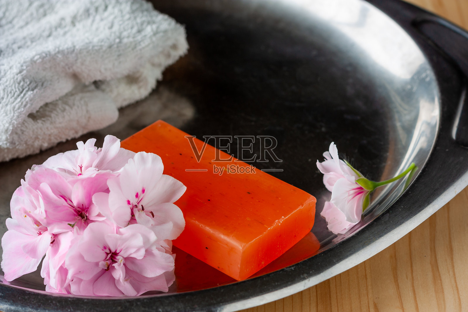手工肥皂与柔软的天竺葵粉红色的花和白色毛巾在钢托盘卫生和水疗照片摄影图片