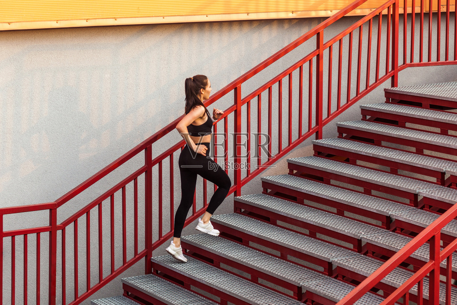 跑步运动员，身材苗条的黑发女孩穿着黑色运动服，紧身裤和上衣，跑上楼梯做有氧运动照片摄影图片