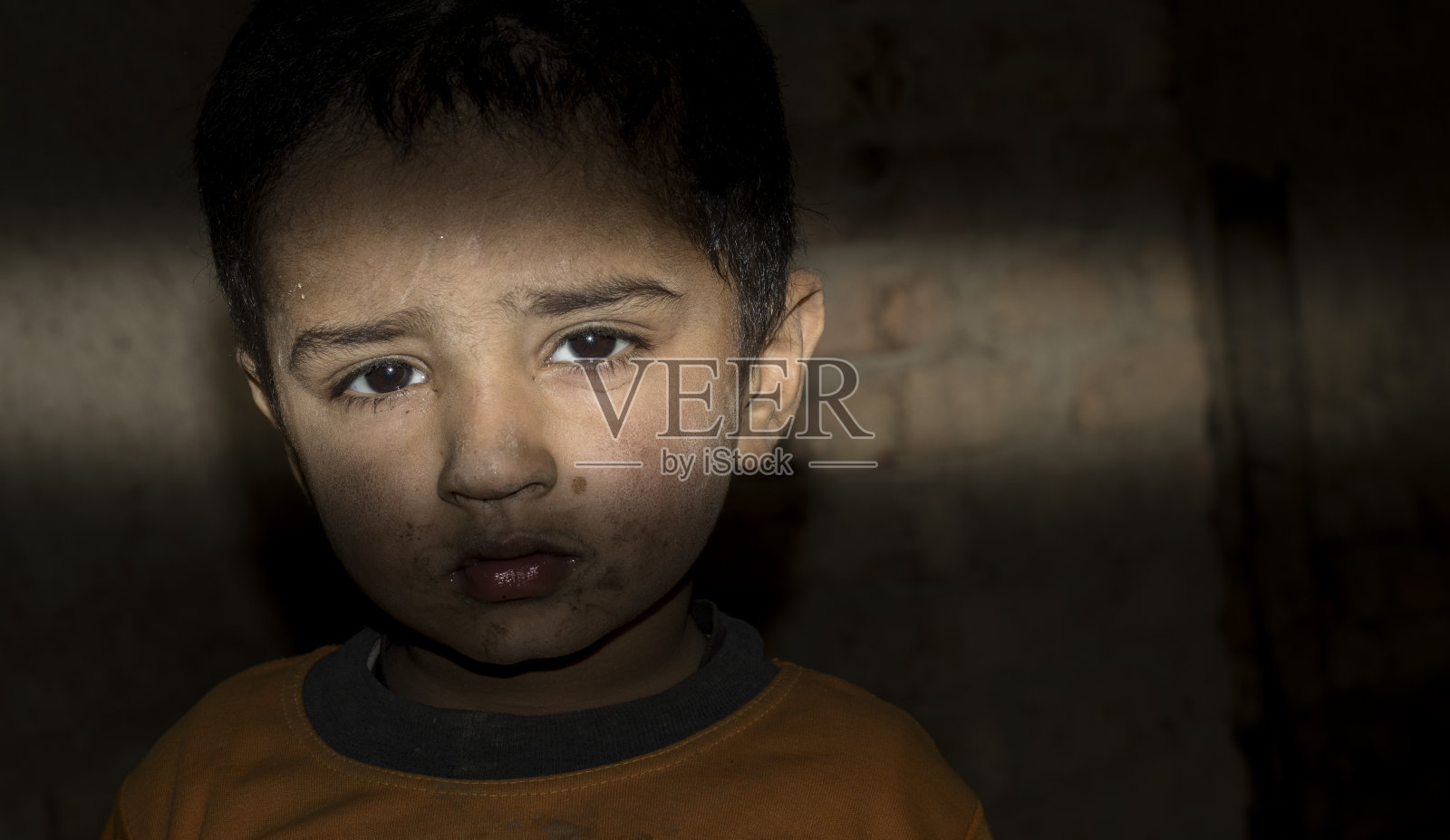 一个无家可归的难民儿童站在黑暗的房间里，脸上带着悲伤的表情照片摄影图片