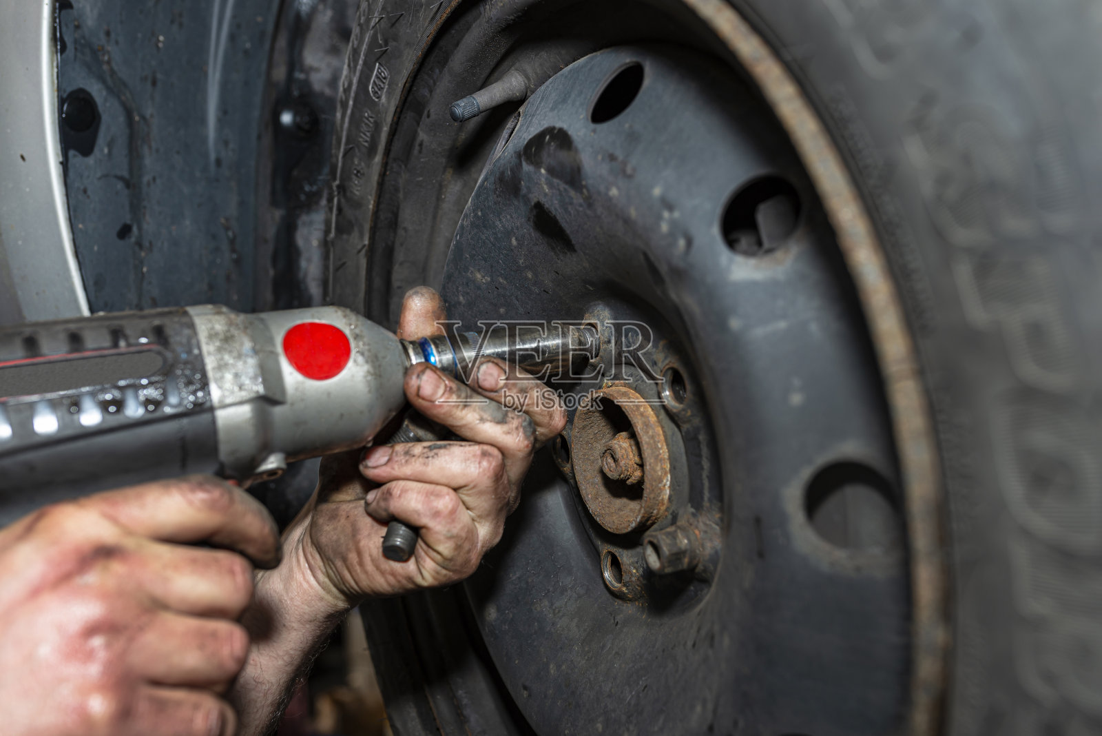 在汽车车间，汽车机械师用气动扳手固定钢制车轮，可见男性的手。照片摄影图片