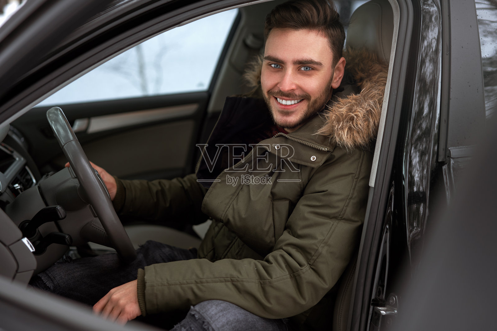 年轻有吸引力的白人男子坐在他的汽车的方向盘阳光明媚的冬天的一天。照片摄影图片