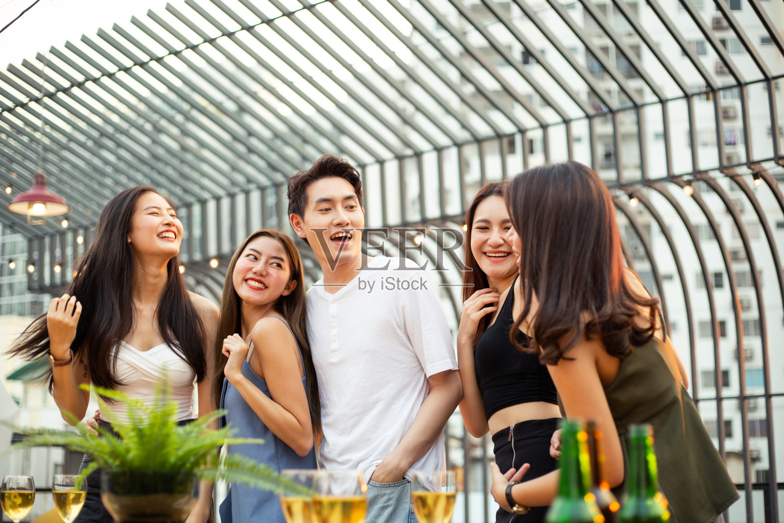一群快乐的亚洲女孩和男人庆祝派对，跳舞和喝在屋顶在日落一起，女帮和男朋友有乐趣，聊天，大笑，年轻人的夜生活方式照片摄影图片