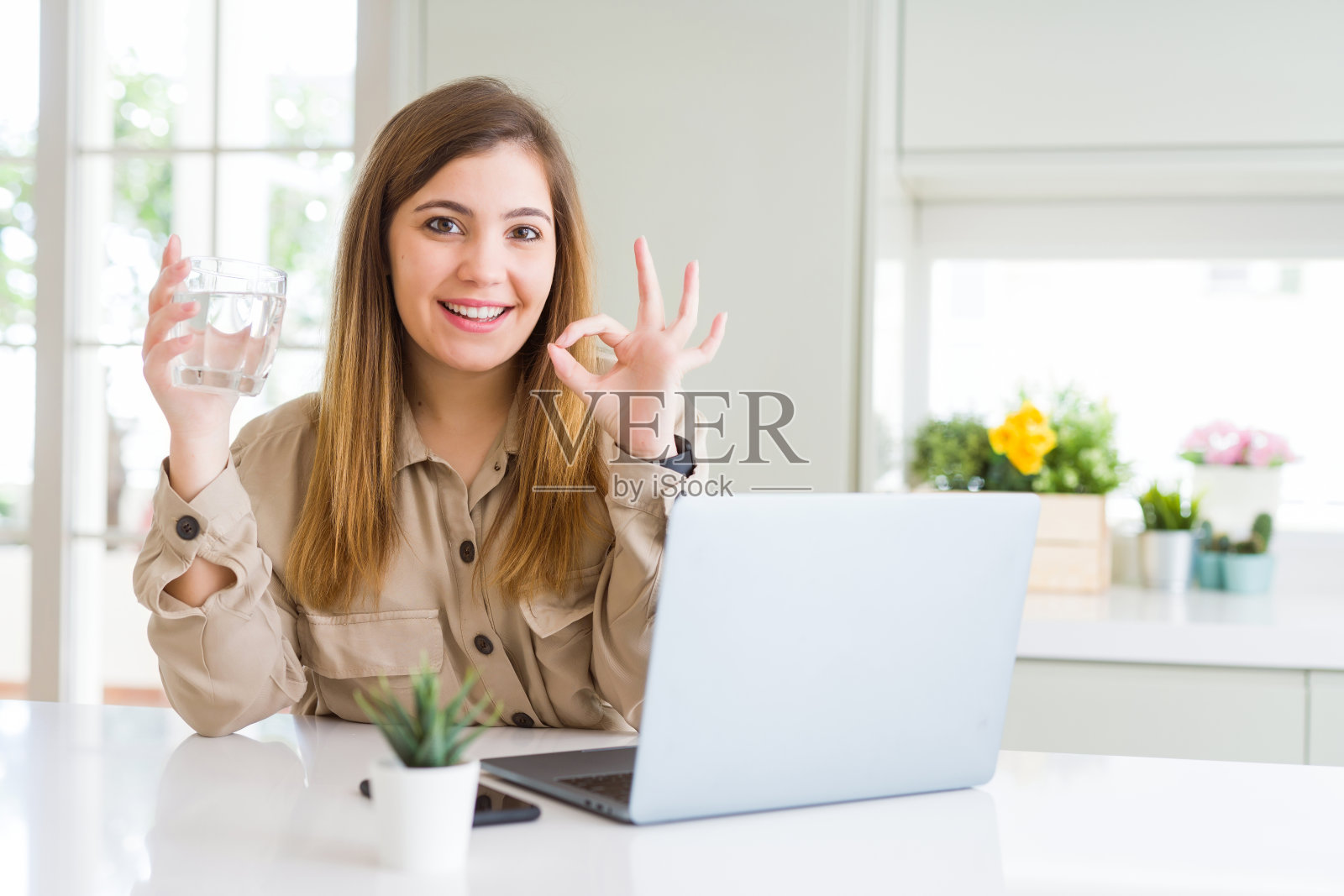 美丽的年轻女子与电脑工作休息喝一杯水做ok手势与手指，优秀的象征照片摄影图片