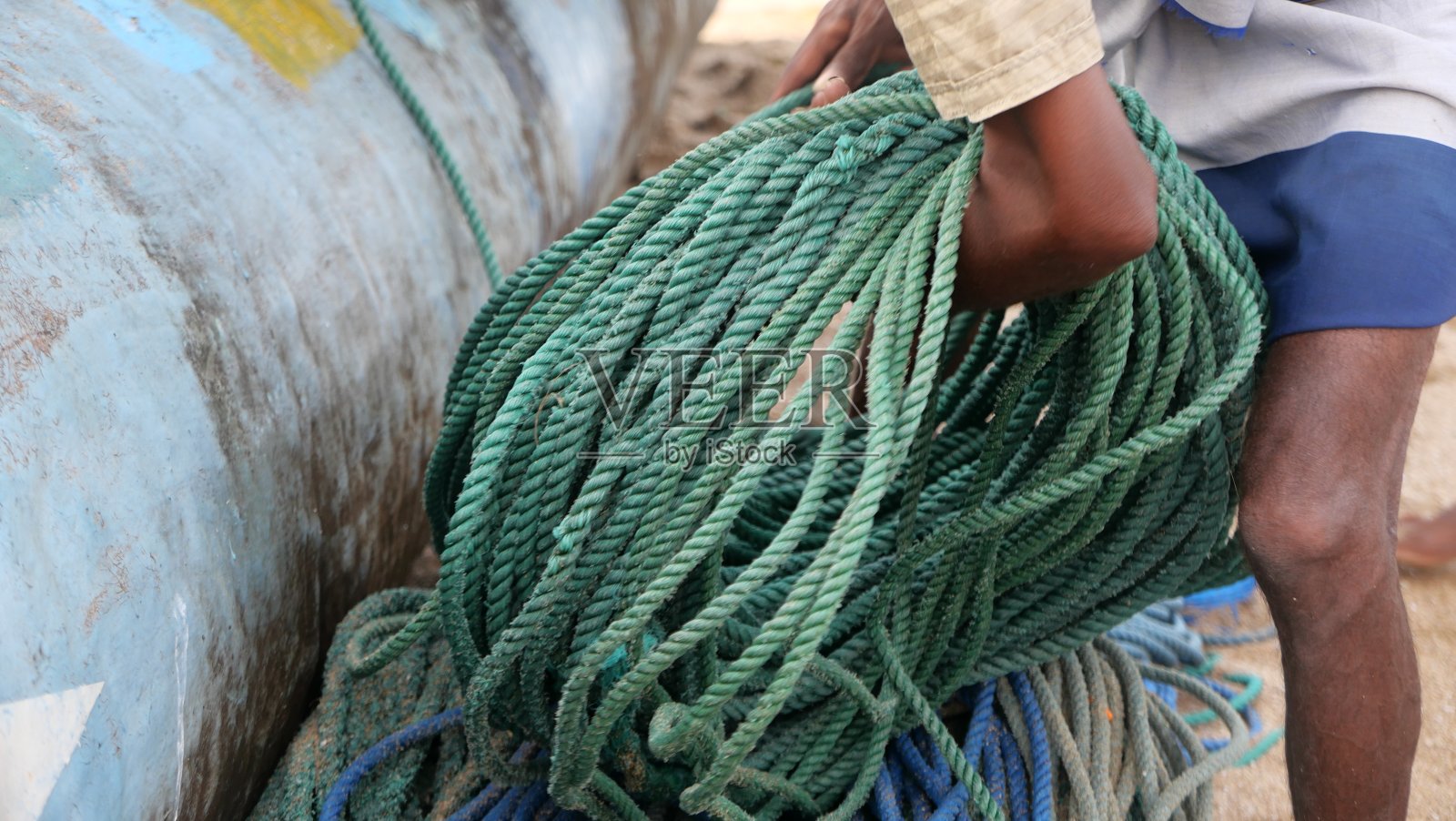 一个渔夫弯腰捡起他渔船旁边的一堆绳子照片摄影图片