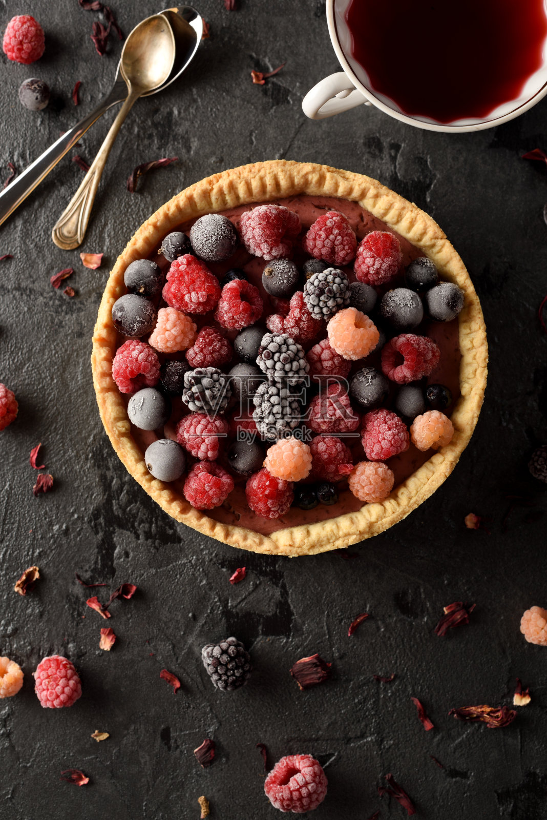 健康糕点的概念。美味的开放派与冰冻的覆盆子，黑莓和黑加仑，木槿茶和干花在黑色的背景照片摄影图片