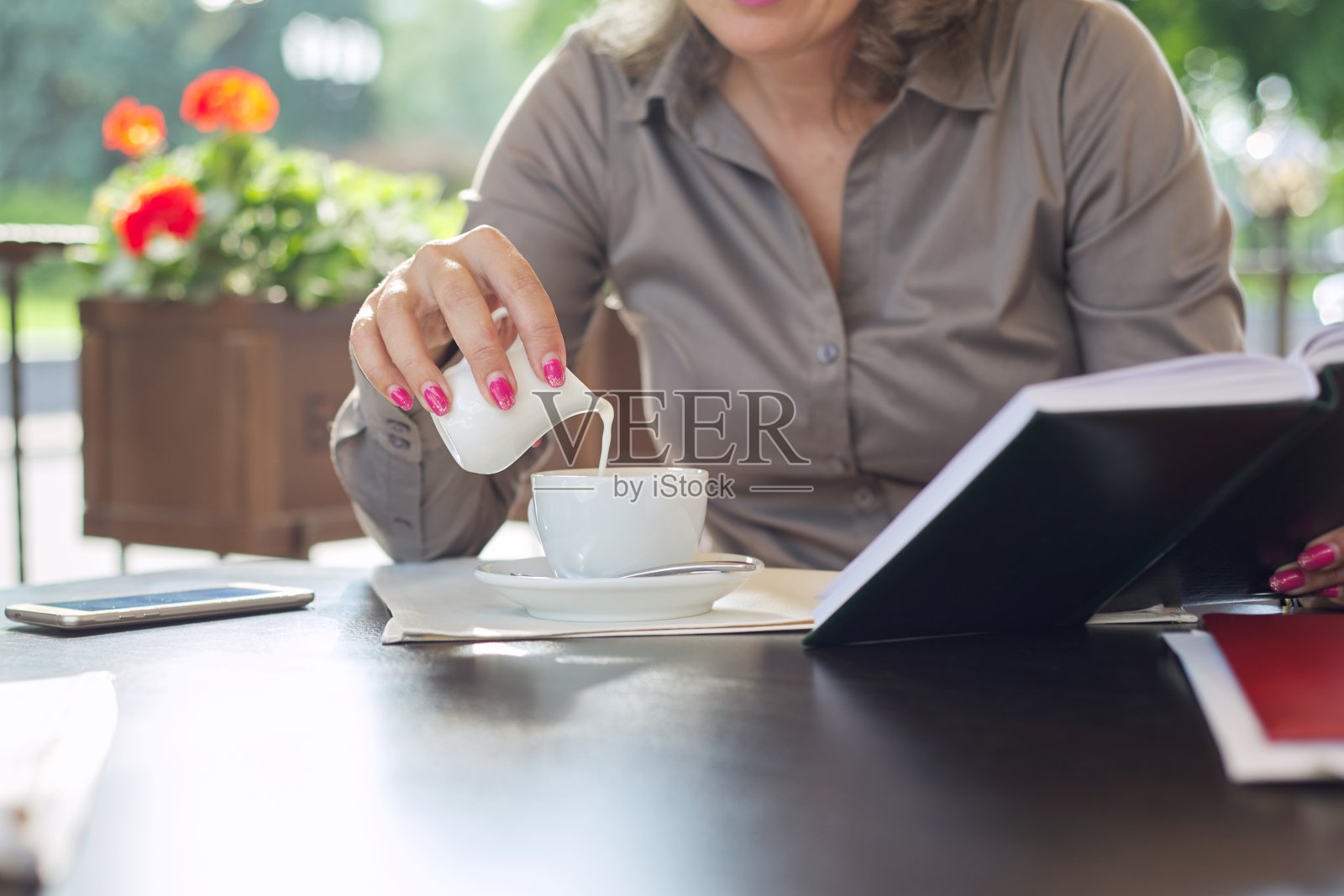 在一家户外咖啡馆里，一位女士正在往一杯咖啡里加牛奶照片摄影图片