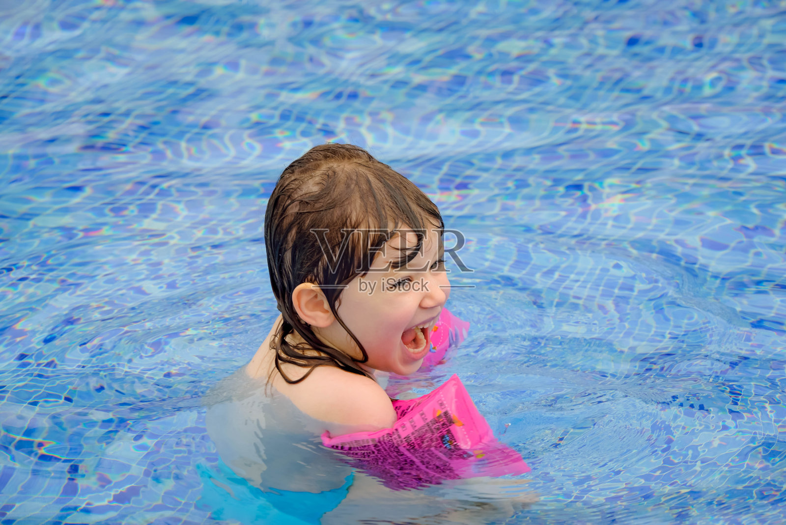 可爱的小女孩戴着臂章在游泳池里玩照片摄影图片