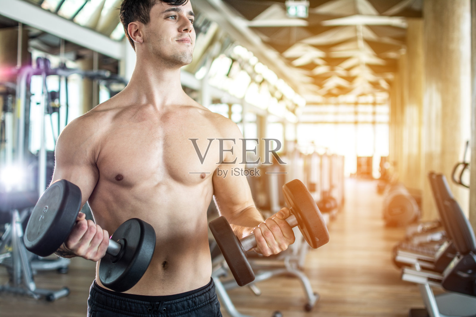 帅气的赤膊举重运动员在健身房用哑铃锻炼。照片摄影图片