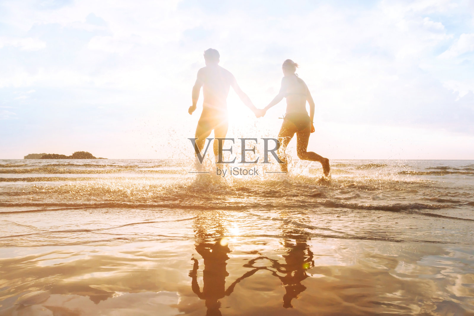 幸福的年轻夫妇在海滩上玩日落，水花照片摄影图片