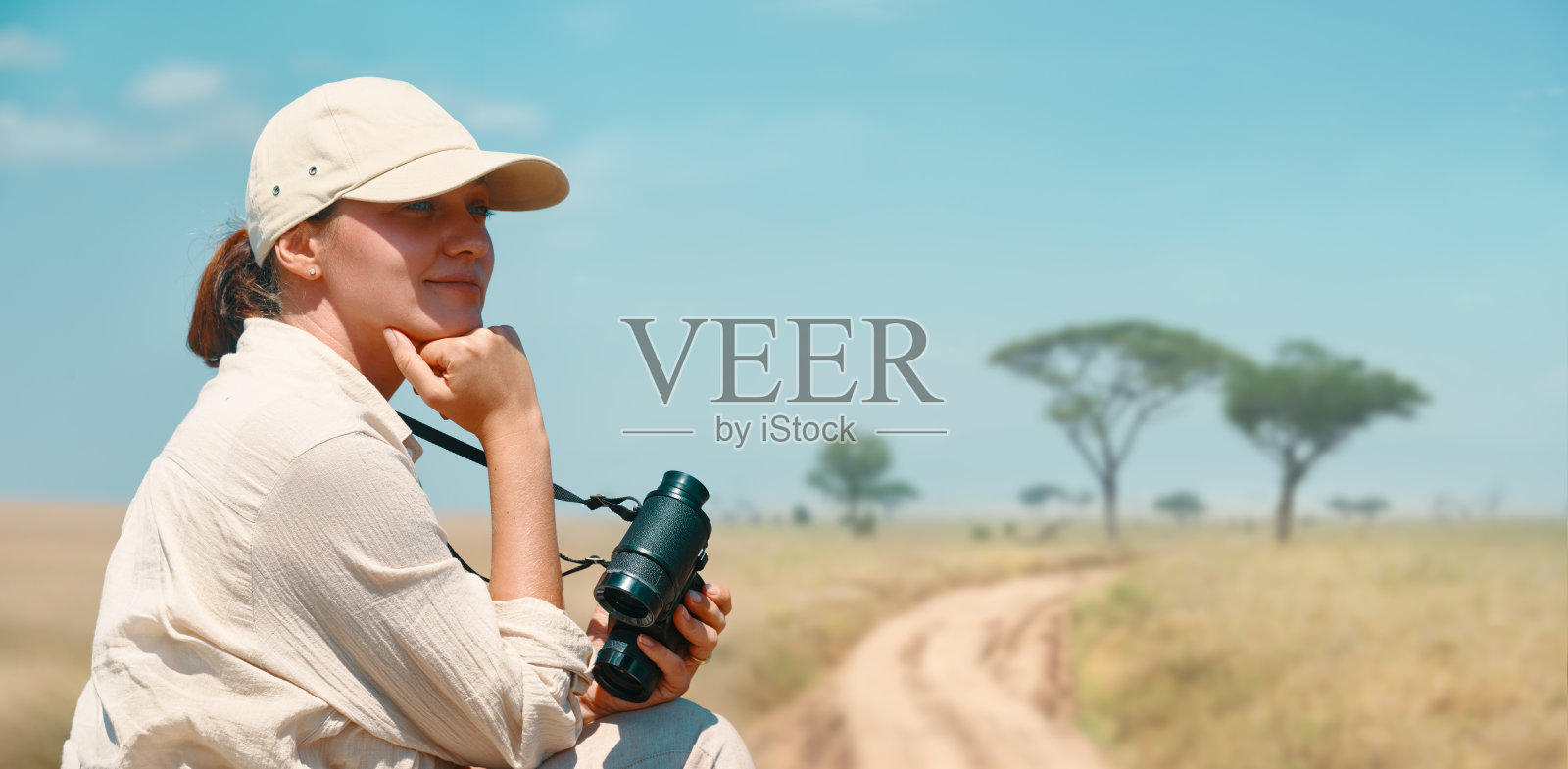 在坦桑尼亚和肯尼亚的一次狩猎之旅中，一名妇女拿着双筒望远镜欣赏非洲大草原的美丽景色照片摄影图片