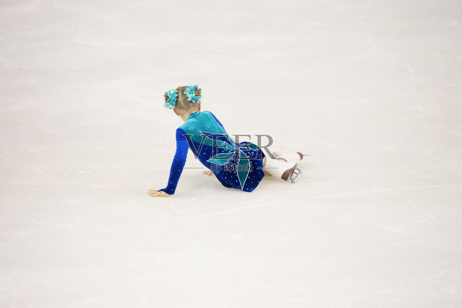 女孩在花样滑冰比赛中。那个小花样滑冰运动员摔倒了照片摄影图片