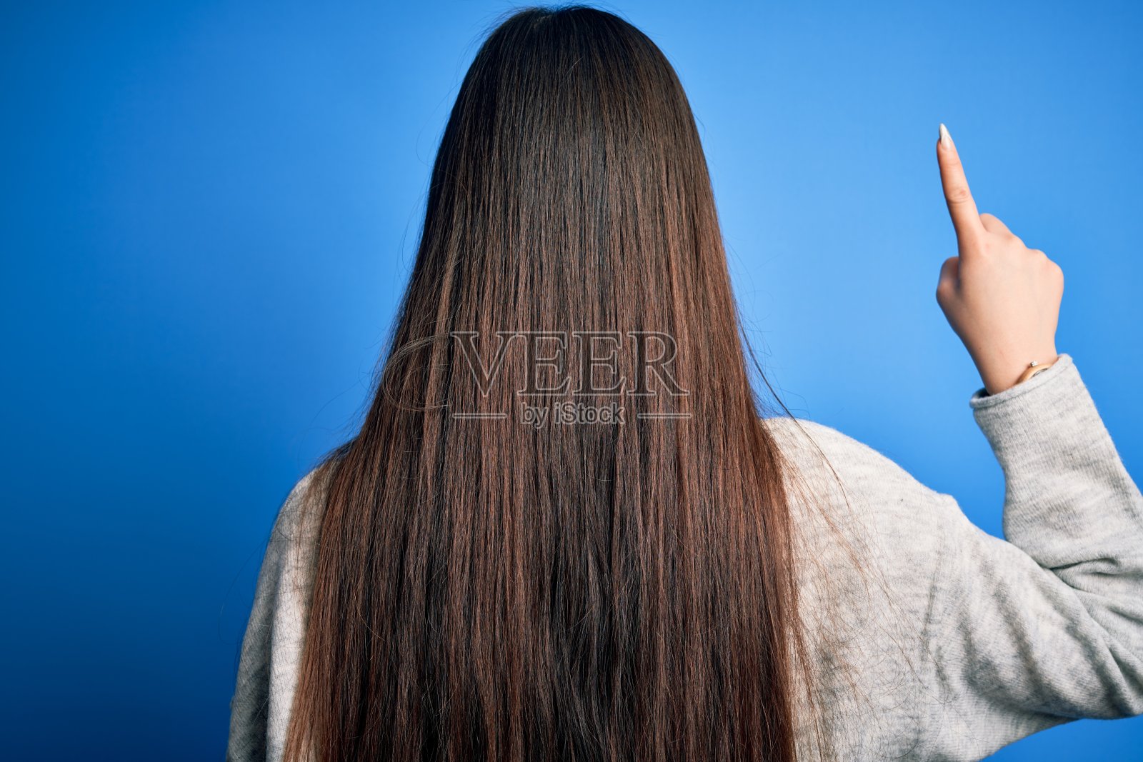 年轻美丽的亚洲女人穿着休闲毛衣站在蓝色孤立的背景摆出向后指向与手指手照片摄影图片