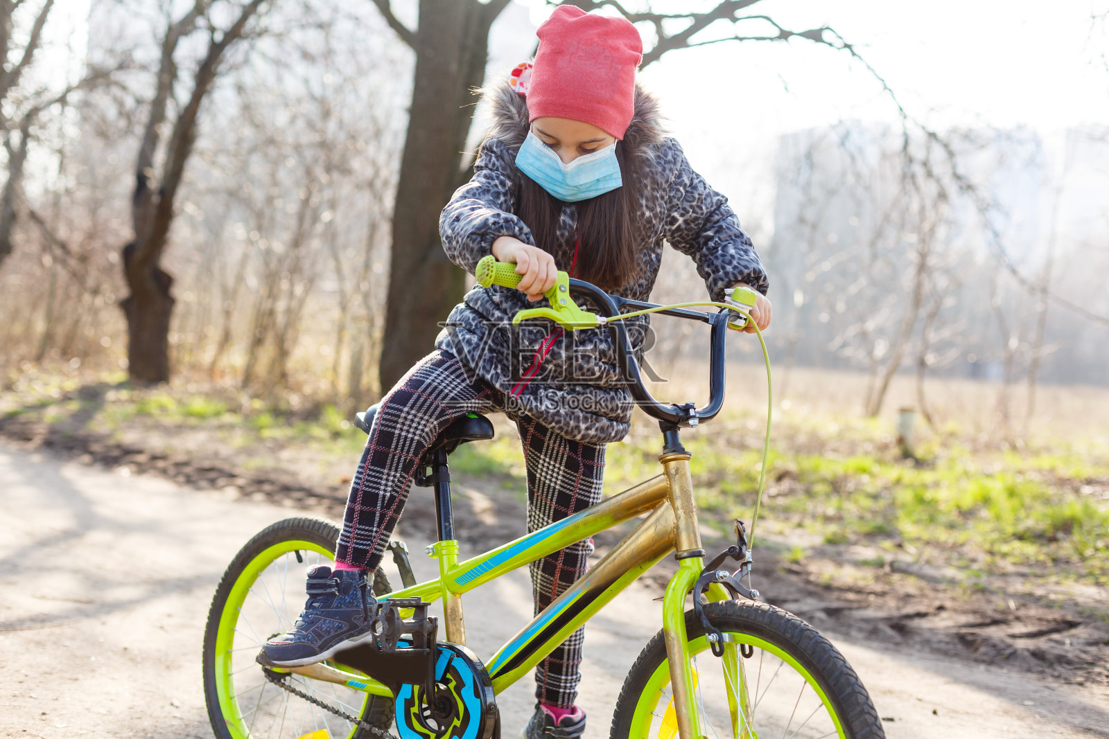 小女孩戴着防污染口罩骑在自行车上。照片摄影图片