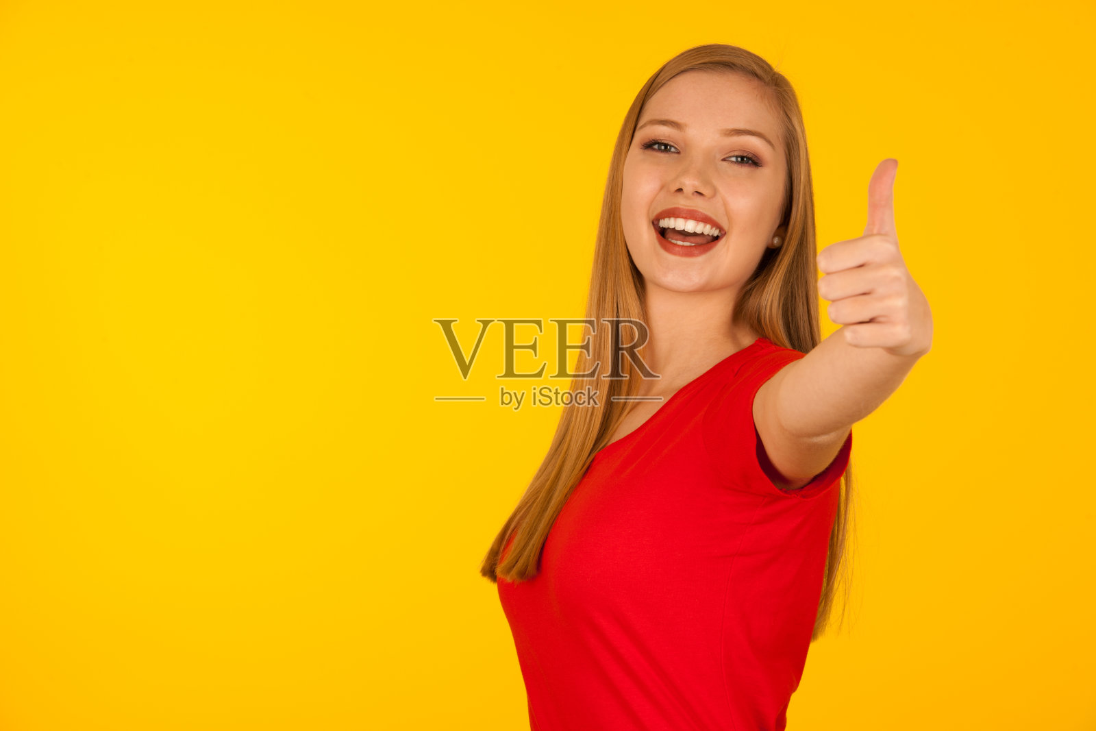美丽的年轻女子在红色t恤在黄色背景显示拇指向上表示成功照片摄影图片