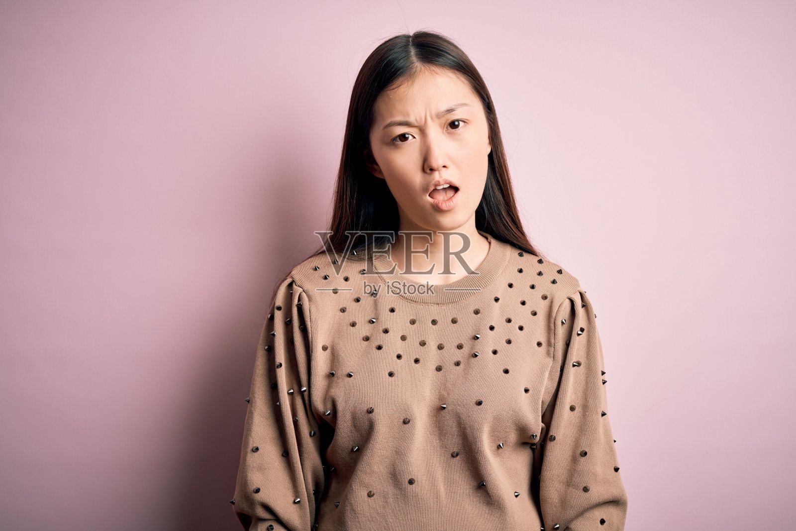 年轻美丽的亚洲女人穿着时尚和优雅的毛衣在粉红色孤立的背景在震惊的脸，看起来怀疑和讽刺，惊讶与张开的嘴照片摄影图片