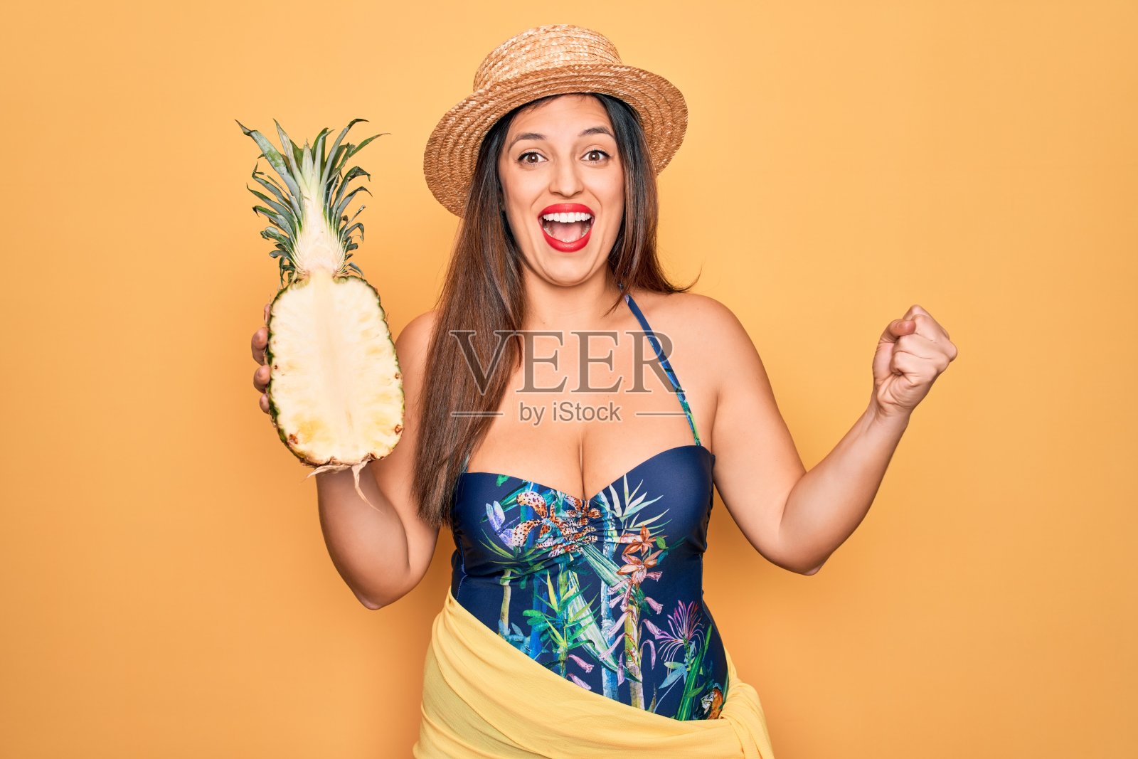 年轻的西班牙妇女戴着夏帽和泳衣，拿着热带菠萝尖叫自豪，庆祝胜利和成功非常兴奋，欢呼的情绪照片摄影图片