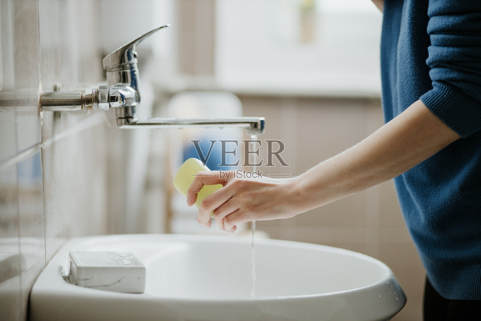 一名妇女在浴室洗手以预防Covid-19病毒感染的特写。在冠状病毒大流行期间，建议使用肥皂和自来水清洗。照片摄影图片