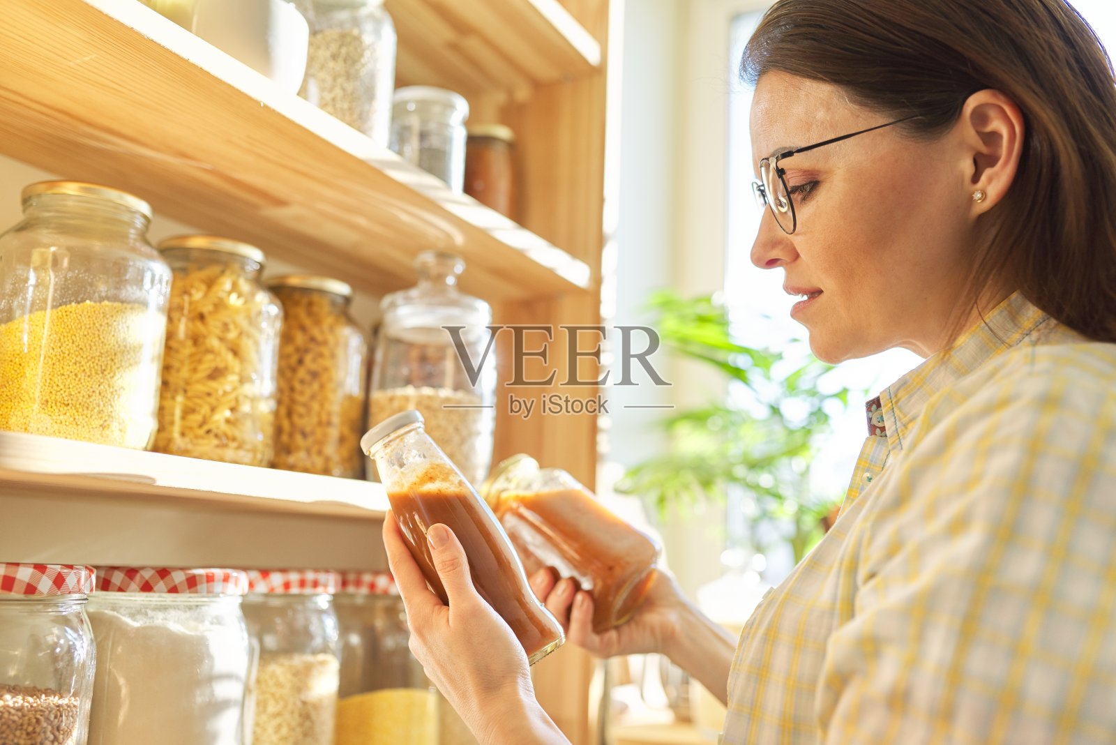 一个女人拿着一瓶番茄酱，从厨房的储藏柜里挑食物照片摄影图片