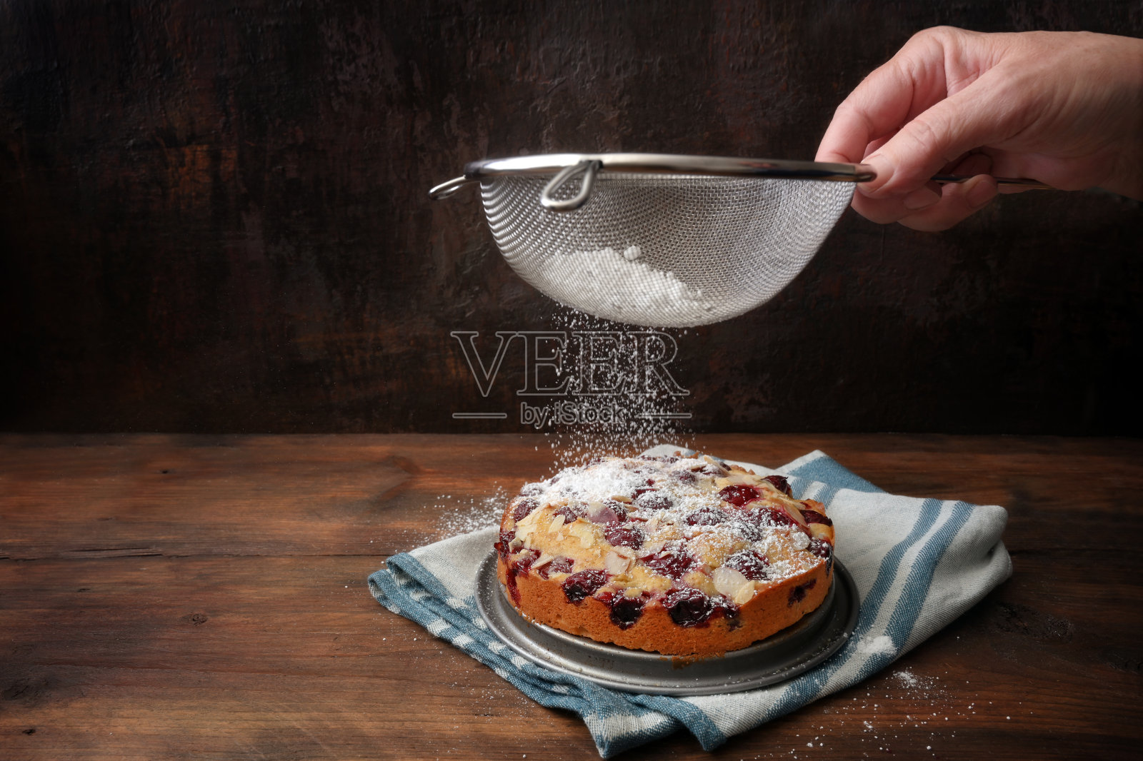 一个女人的手在一个新烤的樱桃小蛋糕上筛糖霜，乡村木材和深色背景与复制空间照片摄影图片