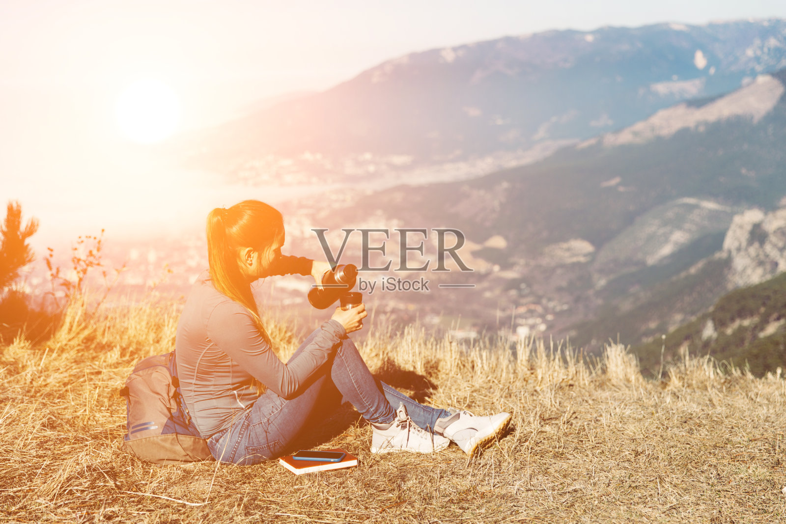 女性旅行的后视图。一个年轻美丽的姑娘在春天或秋天独自在山上旅行，坐在山的边缘，眺望远方照片摄影图片