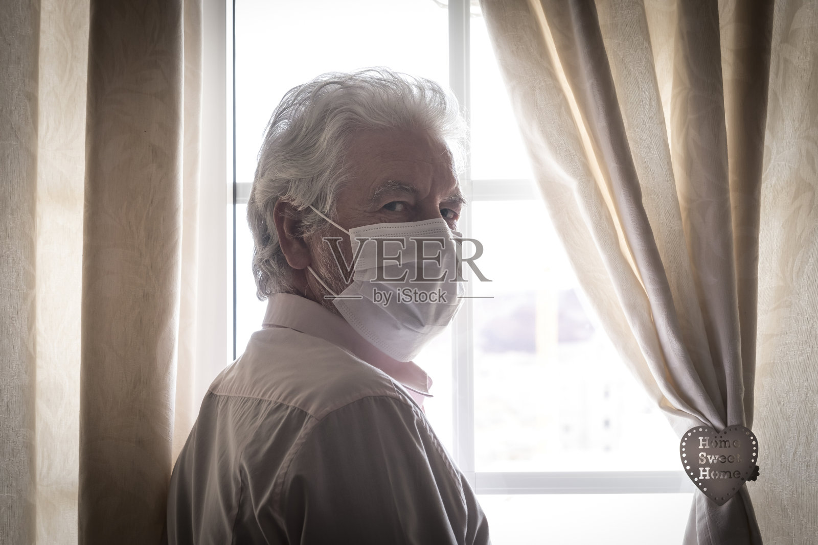 冠状病毒隔离。老人戴着防护口罩躲在窗户后面，避免被COVID-19传染——责任和预防理念照片摄影图片