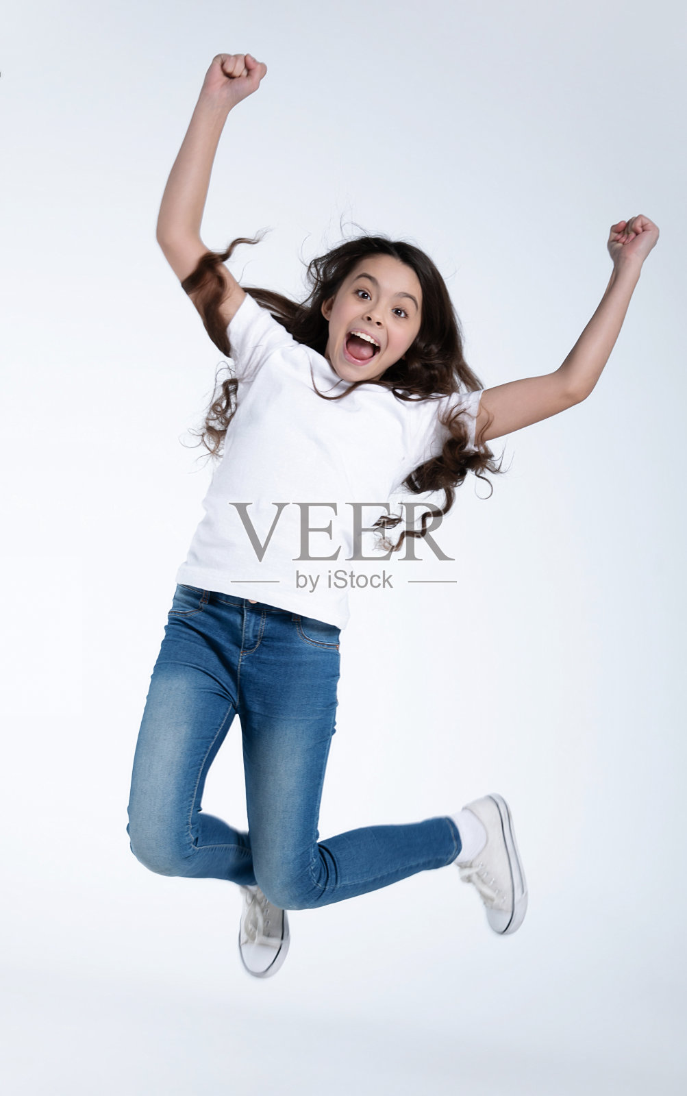 兴奋和快乐的小女孩在白色t恤和牛仔裤上跳和喊孤立的白色背景。照片摄影图片