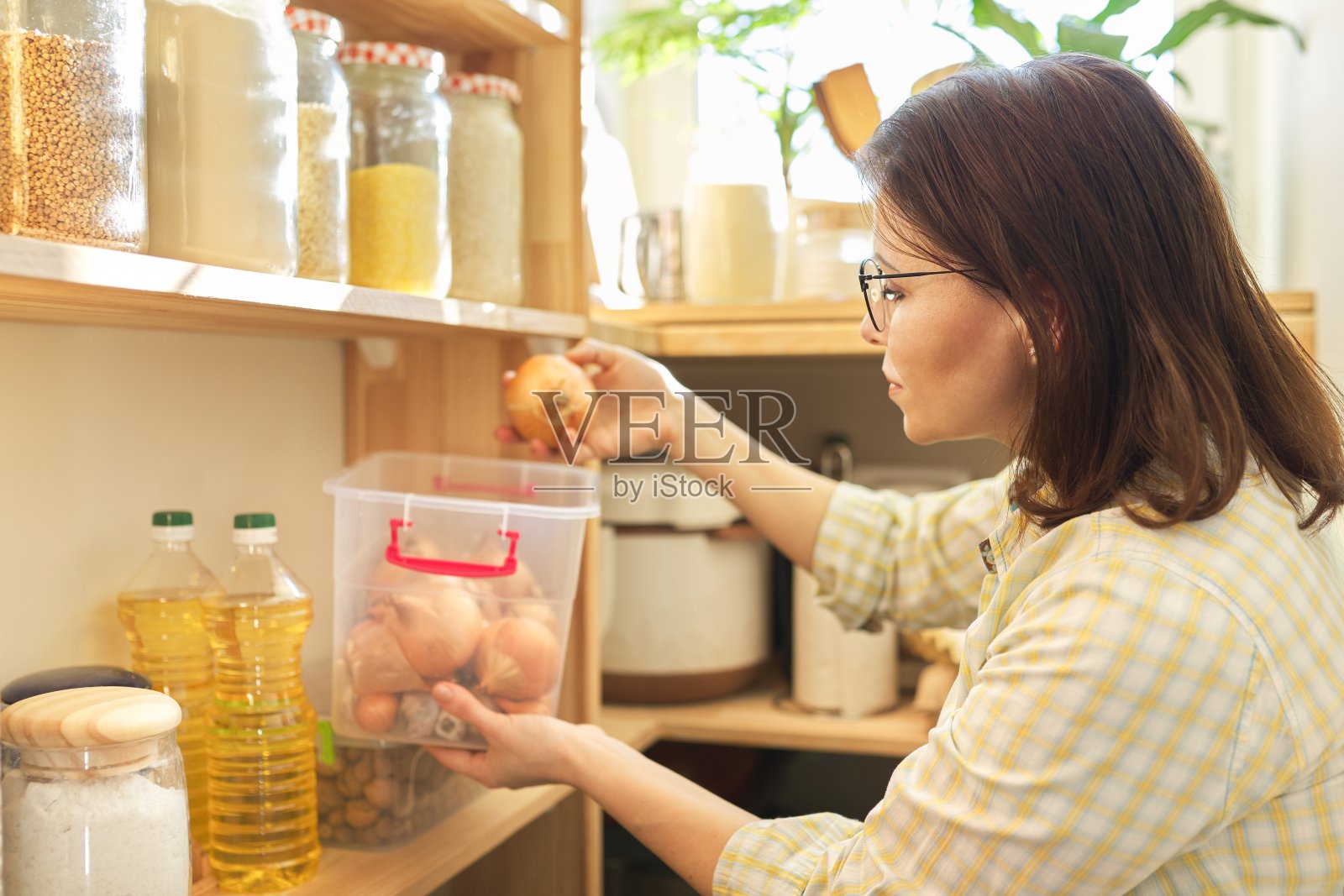 妇女在食品储藏室拿着洋葱，食物存放在食品储藏室的木架上照片摄影图片