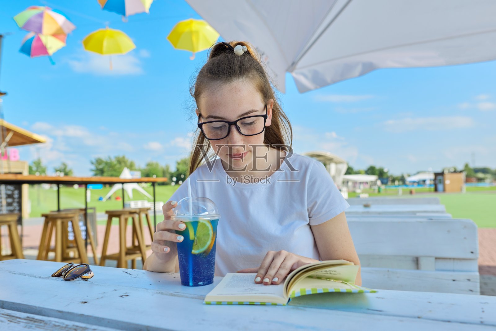 夏天的肖像十几岁的女孩在眼镜看书，女孩坐在咖啡馆与鸡尾酒照片摄影图片