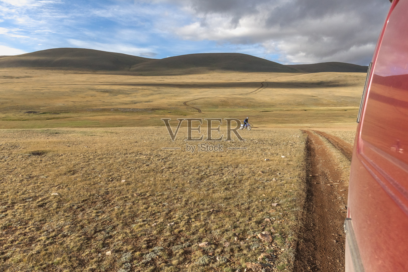 戴头盔的摩托车手骑着摩托车跟在汽车后面。阿尔泰山，蒙古的群山照片摄影图片
