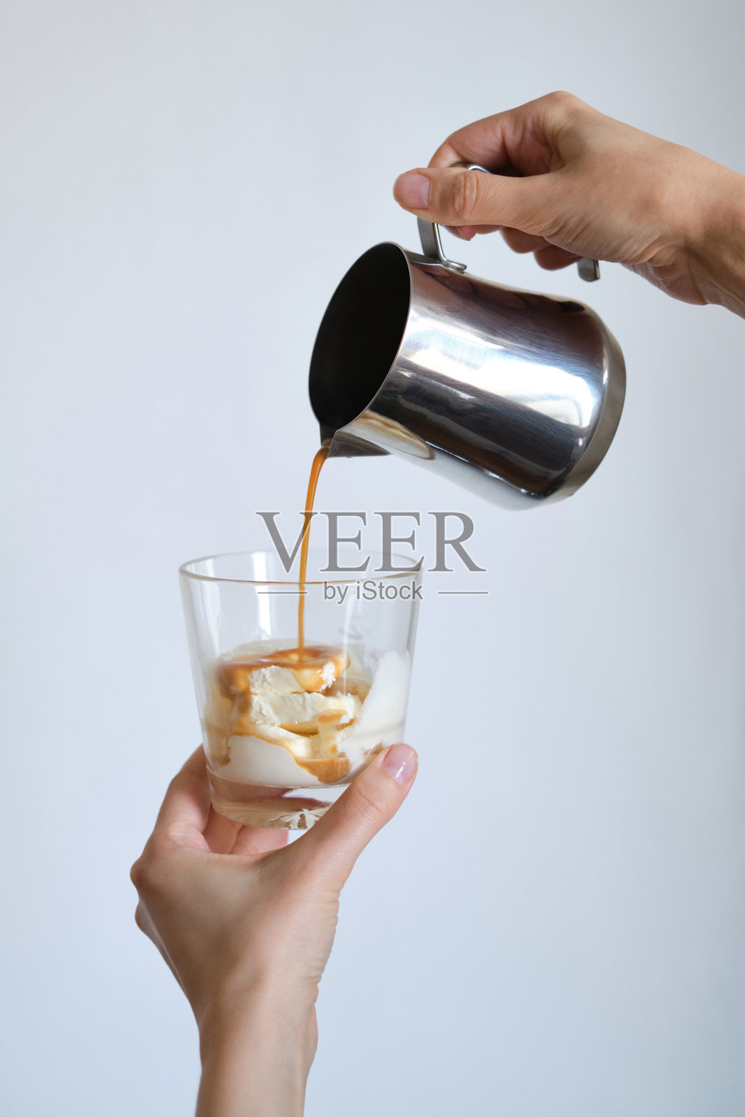 一个女孩将热的意式浓缩咖啡从牛奶罐里倒入一杯冰淇淋中。女咖啡师正在制作美味的咖啡饮料。甜蜜的液体沙漠。金属牛奶罐。咖啡的房子。专业的服务照片摄影图片