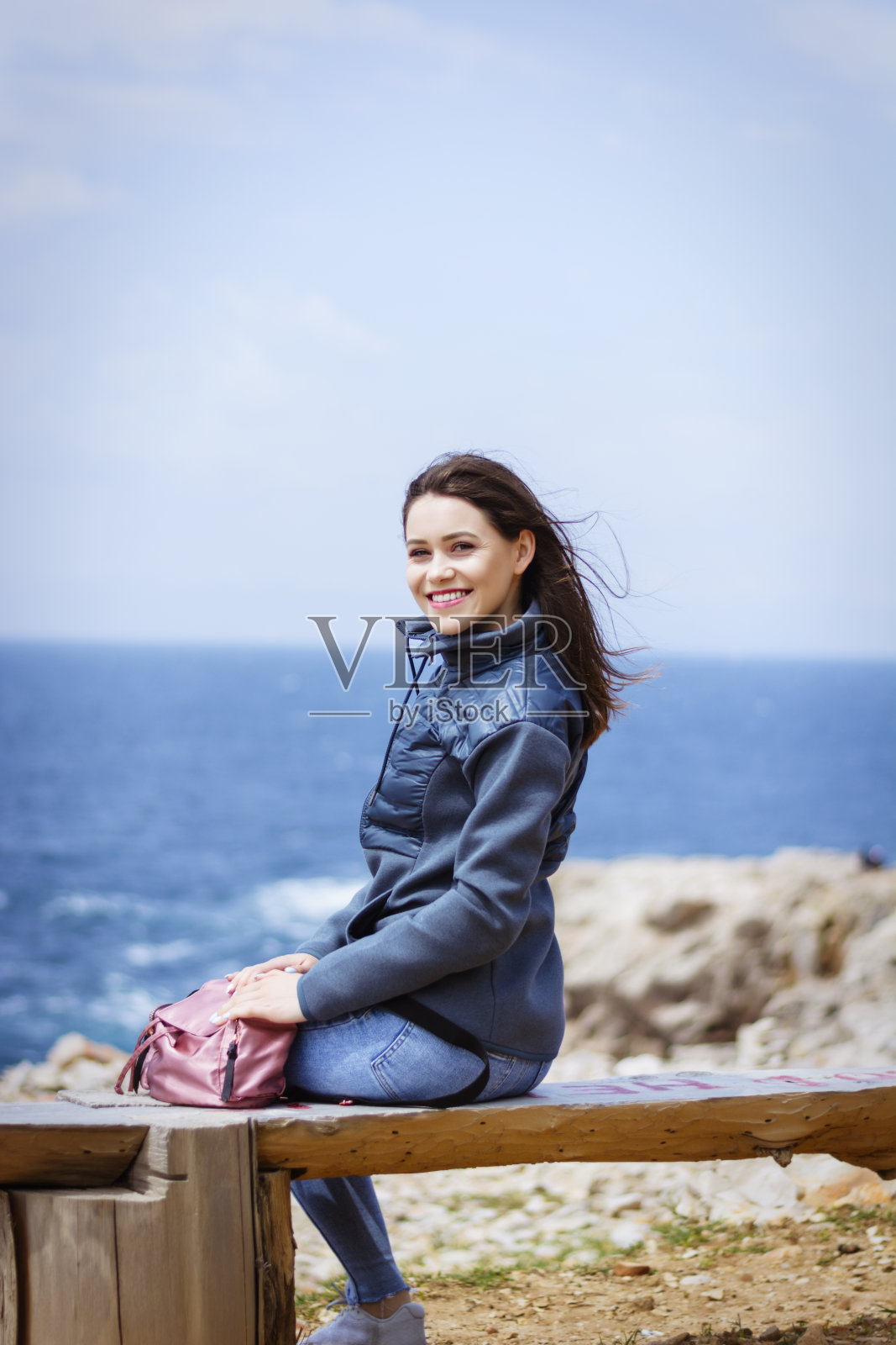 年轻美丽的女人坐在海边的岩石上照片摄影图片