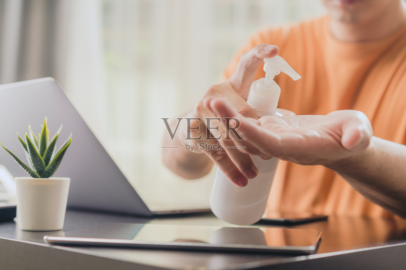 亚洲男子在家工作时使用笔记本电脑后用酒精凝胶洗手。被隔离的男性用抗菌洗手液洗手照片摄影图片