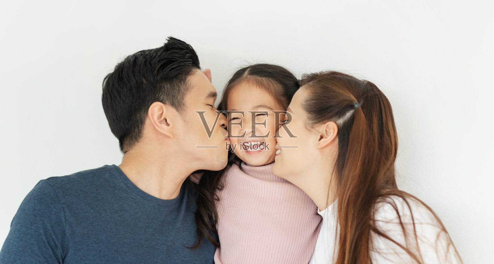 亚洲的家庭快乐。年轻的爸爸和妈妈一起亲吻女儿的脸颊。照片摄影图片