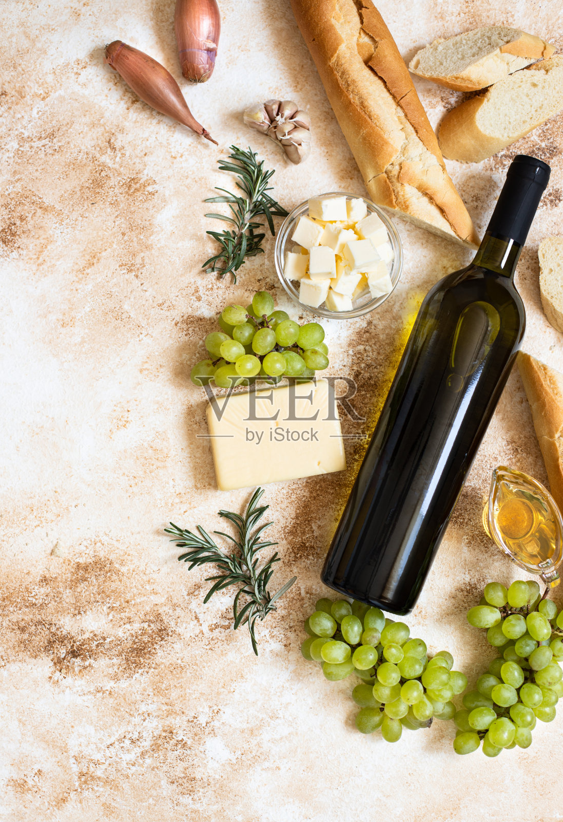 一瓶白葡萄酒，葡萄，奶酪，黄油，蜂蜜，长棍面包，葱和迷迭香。白葡萄酒和法国菜的概念。平铺，复制空间，浅色大理石背景照片摄影图片
