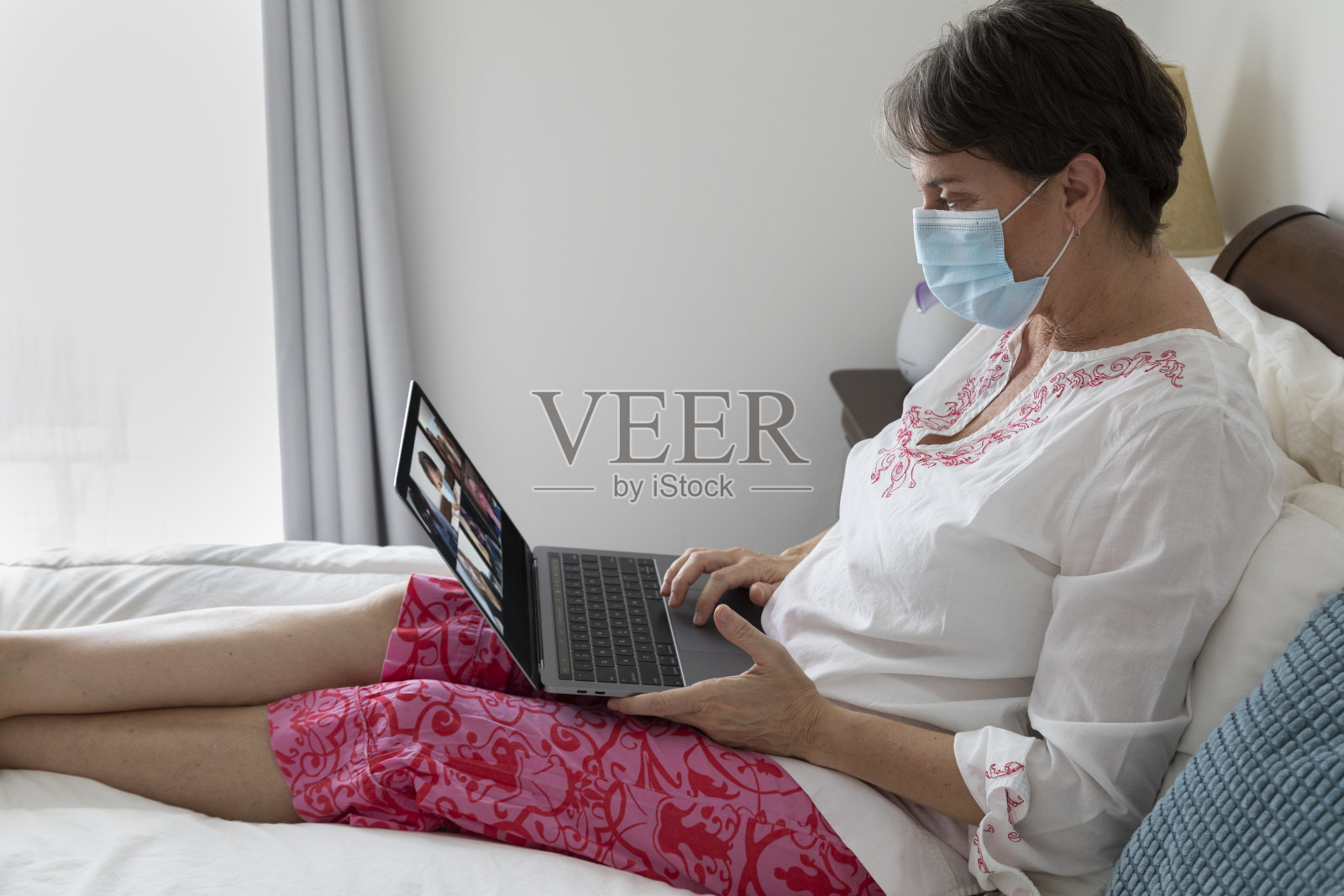 妇女生病在床上戴着口罩用笔记本电脑群视频聊天照片摄影图片