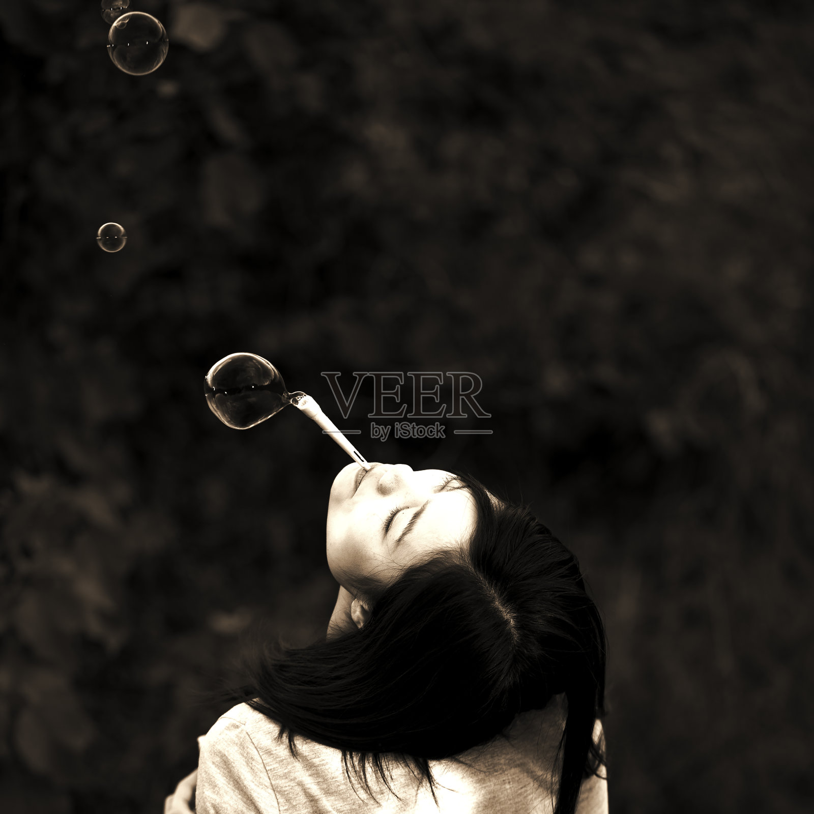 一个年轻的女人面朝上吹肥皂泡。照片摄影图片