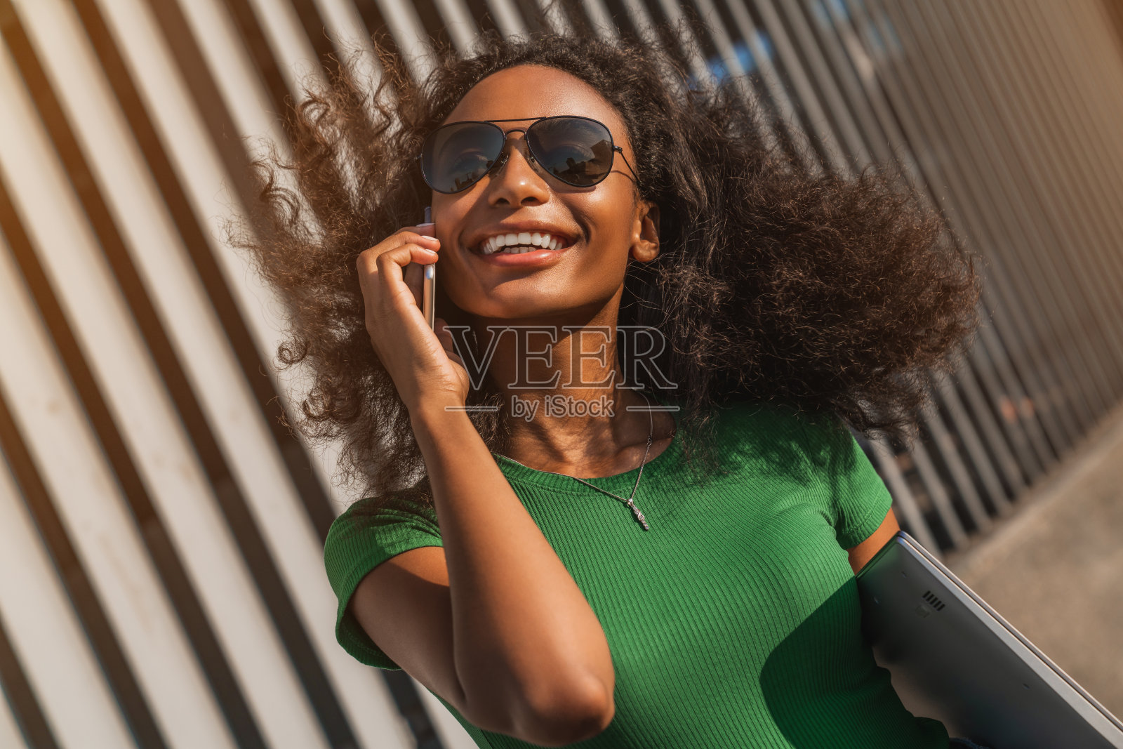这是一幅年轻非洲妇女的肖像，她一边走一边笑，手里拿着手机和笔记本电脑照片摄影图片