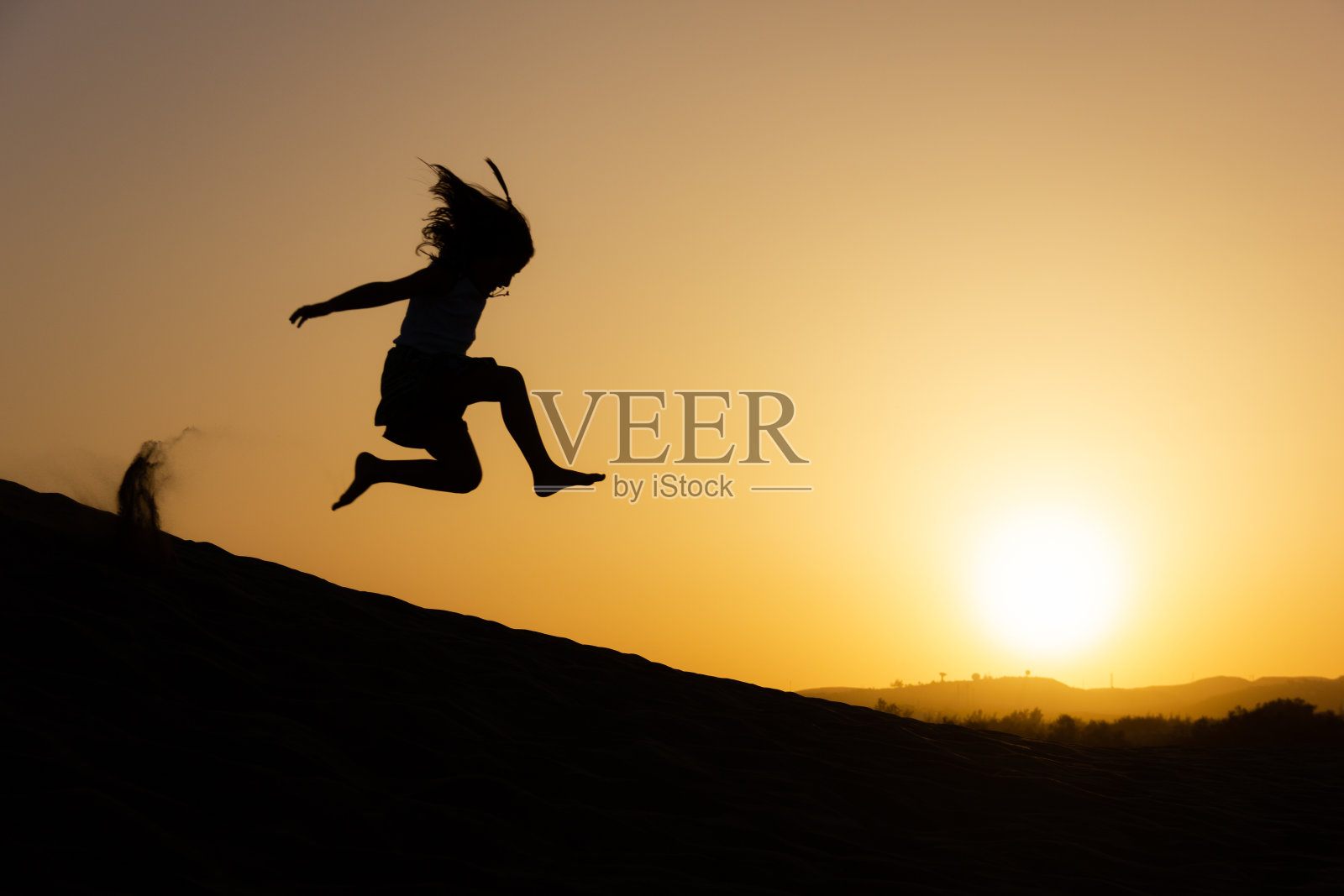 在大加那利岛马斯帕洛马斯，一个小女孩在夕阳下跳过沙丘照片摄影图片
