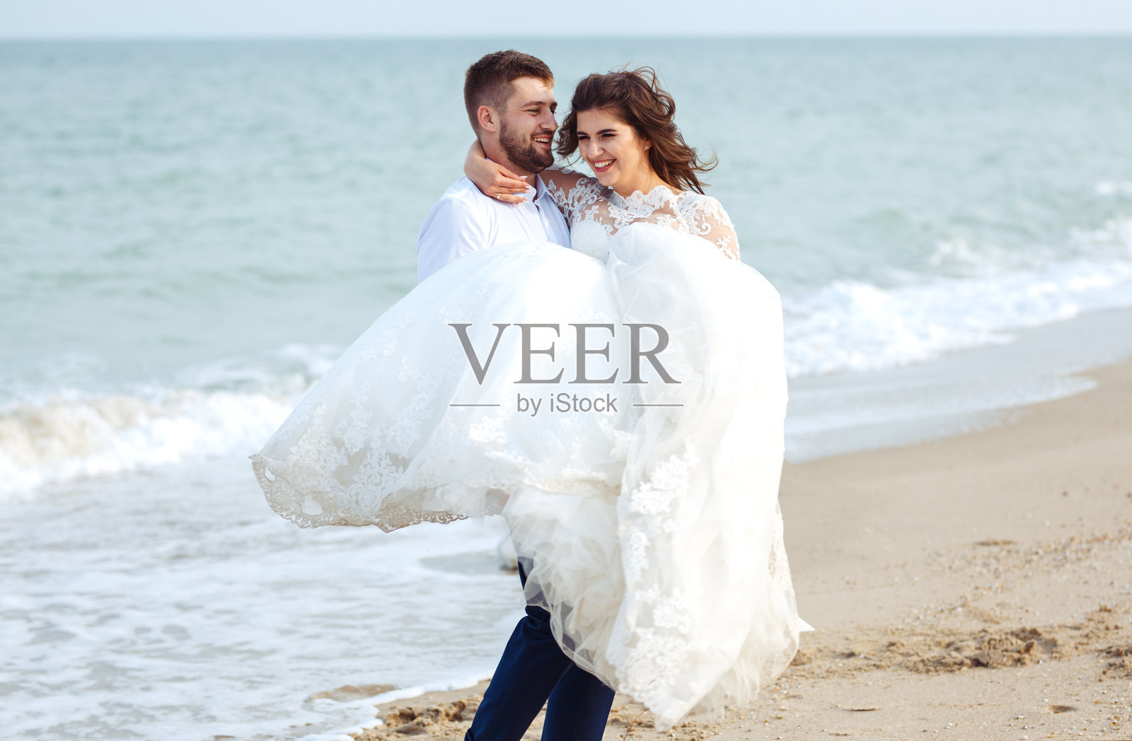 美丽的新娘和新郎享受彼此沿着海滩散步。照片摄影图片