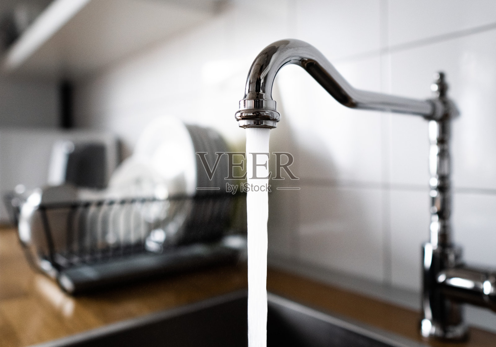 水从厨房的不锈钢水龙头流出，流入水槽。让镀铬的水龙头一直开着浪费水。过度使用家庭用水。在家务和活动中误用水。照片摄影图片