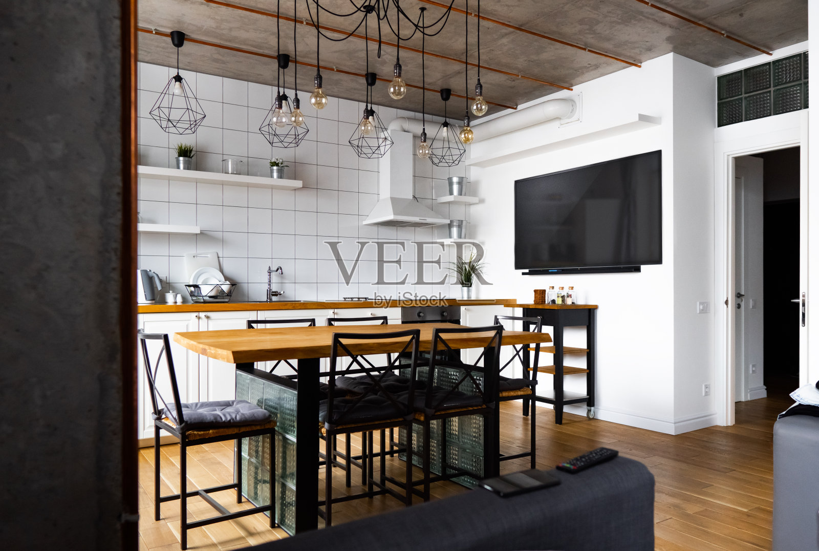 现代斯堪的那维亚风格的厨房室内设计，宽敞的木桌和椅子，浅色木地板，明亮的白色墙壁和家具，电视，电器和悬挂灯泡照片摄影图片