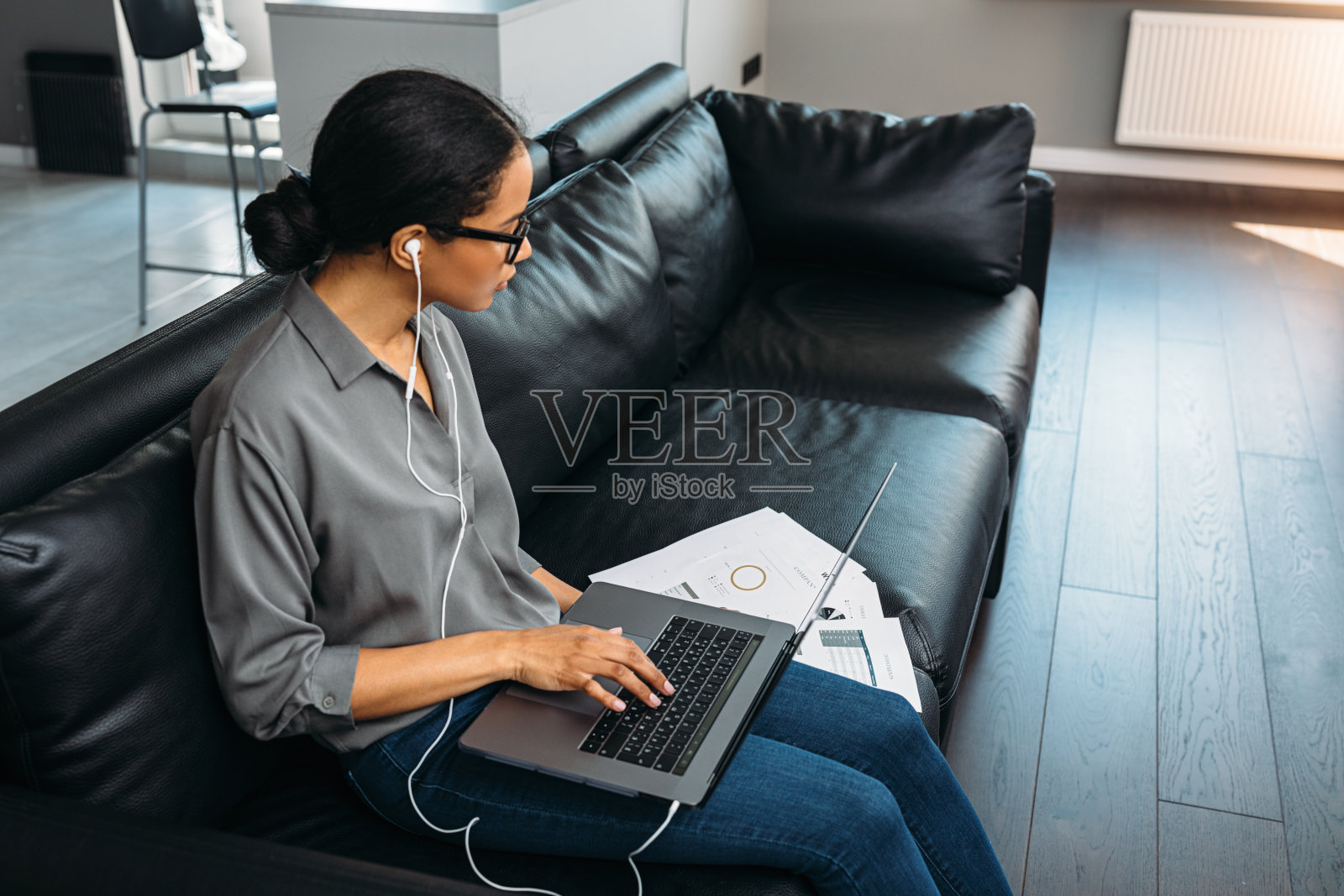 一个年轻女子坐在她公寓客厅的沙发上，用笔记本电脑看文件照片摄影图片