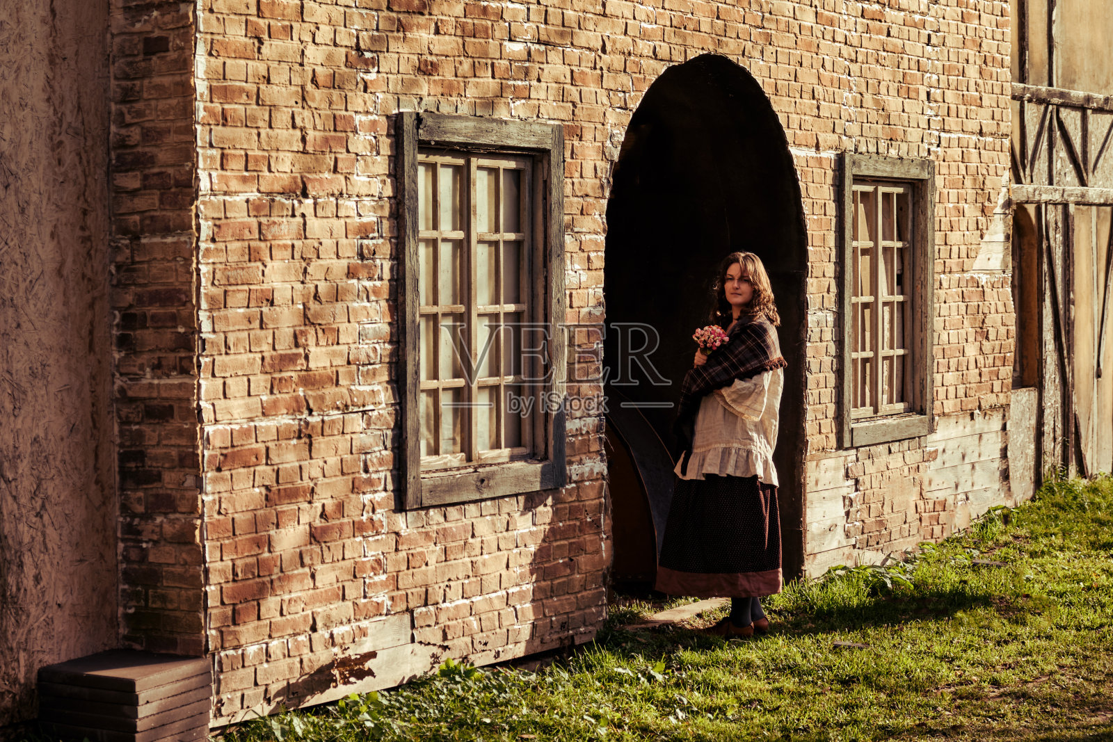 一个穿着古装的女人站在复古屋的拱门前。欧洲中世纪的建筑照片摄影图片