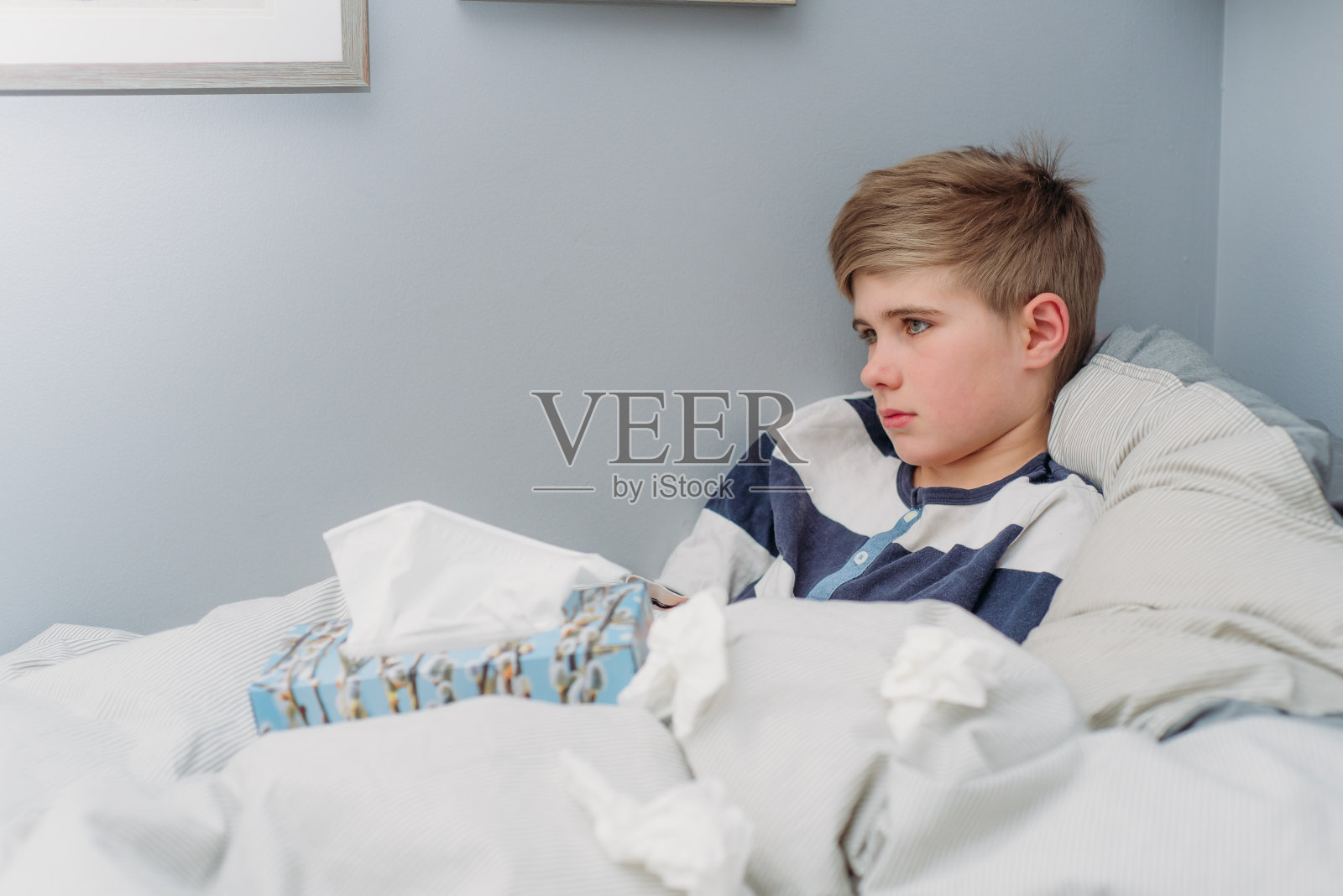 一个10岁的男孩躺在白色和灰色的床上。照片摄影图片