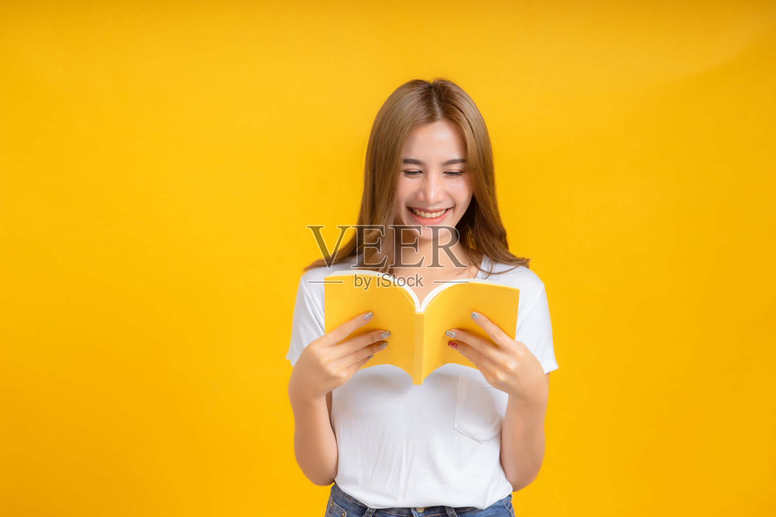 肖像年轻快乐的亚洲妇女阅读书籍教育学习知识微笑积极的情绪在白色t恤，黄色背景孤立的工作室拍摄和复制空间。照片摄影图片