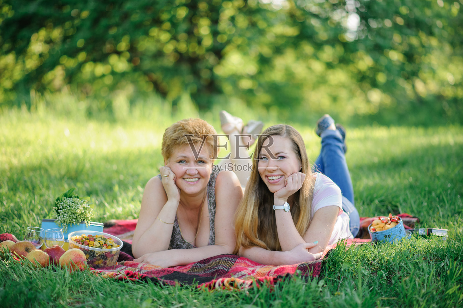 一个成年的女儿和她的老母亲一起躺在公园里的一块格子布上。照片摄影图片