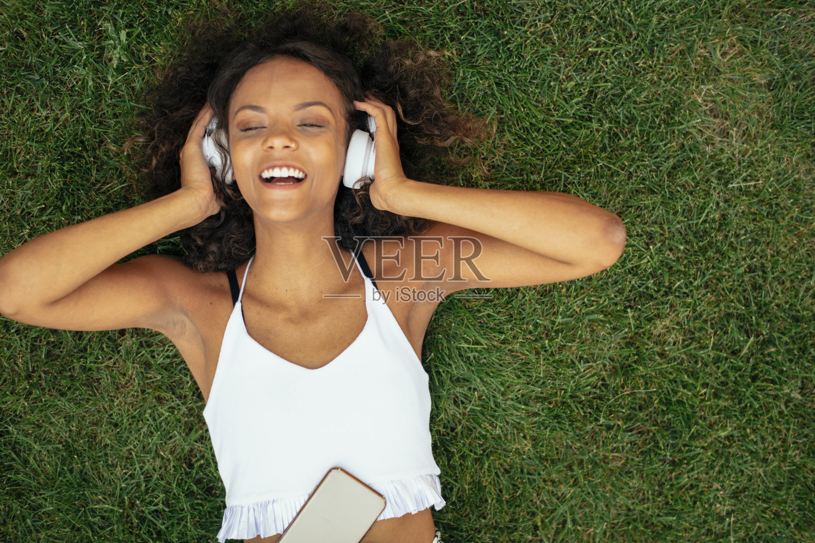 年轻的非洲女孩躺在草地上听着音乐照片摄影图片