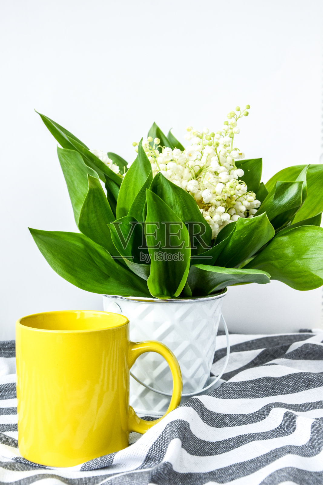 白色的桌子上放着黄色的茶杯，上面放着一束铃兰。假日背景概念照片摄影图片