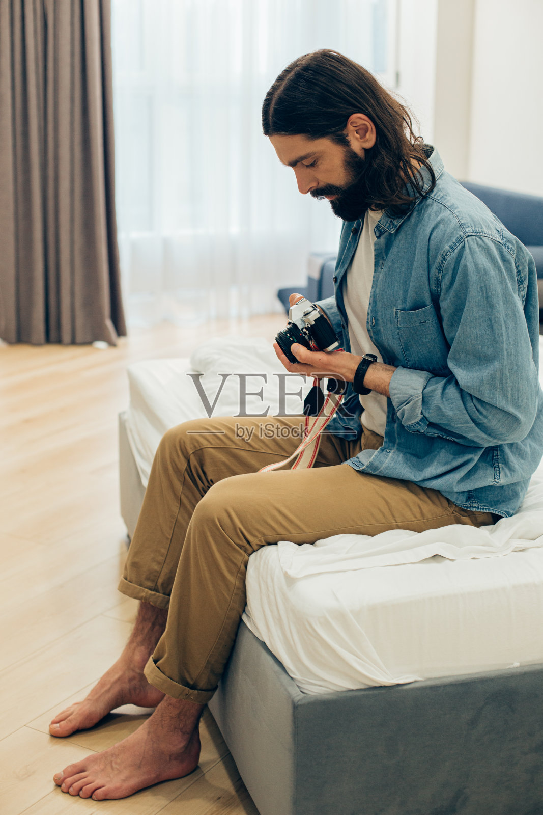 一个冷静的男人，拿着相机坐在家里的床上照片摄影图片